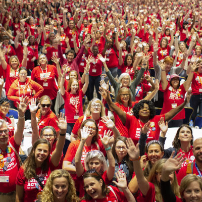 A large crowd of Moms Demand Action volunteers raise their arms in the air at the Gun Sense University conference