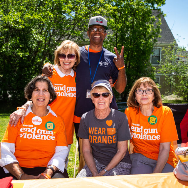 A group of three women in 'we can end gun violence' shirts pose for a photo with a man in a baseball cap
